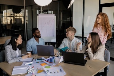 A team of colleagues meets around a conference table reviewing data as a leader presents a line graph, illustrating collaboration and decision‑making during organizational change.