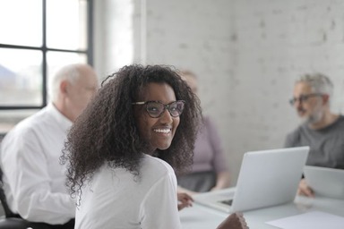 A young professional smiling confidently in a business meeting, representing the value of asking is a master's in management worth it for early-career growth.